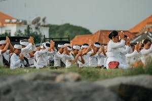 Group of Balinese people engaged in a traditional prayer ceremony outdoors.