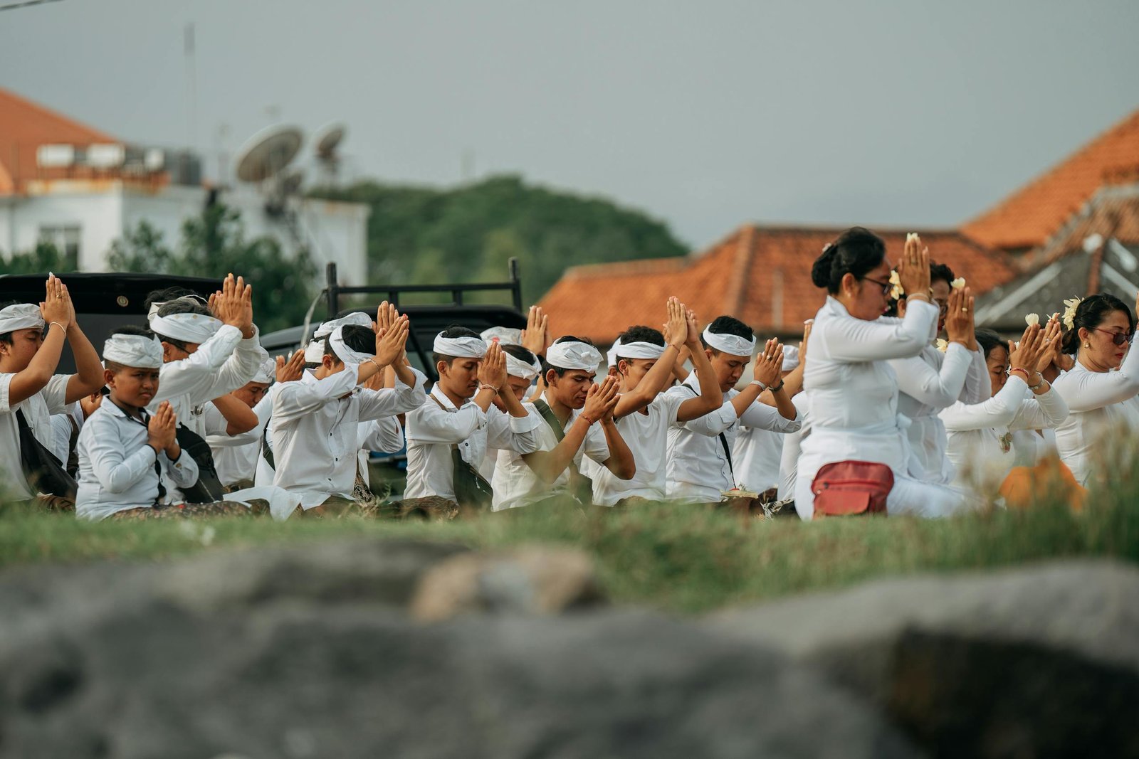 Group of Balinese people engaged in a traditional prayer ceremony outdoors.