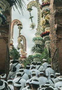 A traditional Balinese ceremony with people in white attire entering a temple adorned with ornate decorations.