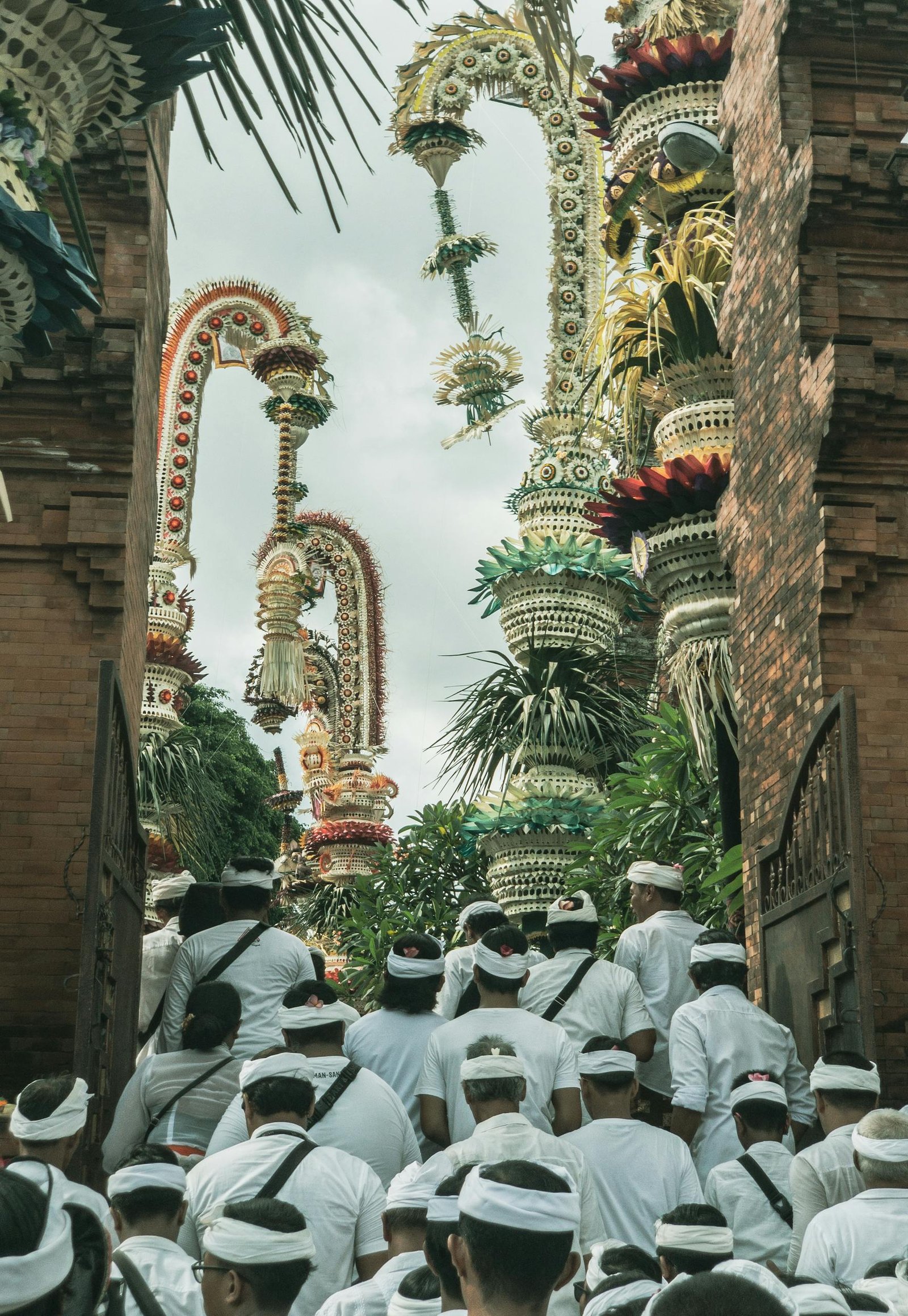 A traditional Balinese ceremony with people in white attire entering a temple adorned with ornate decorations.