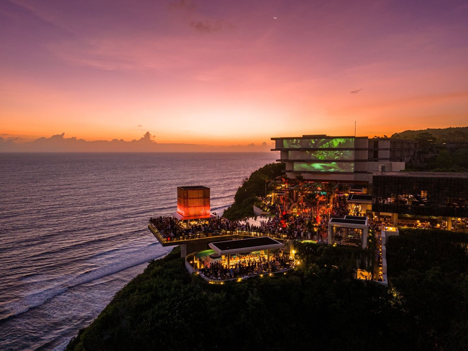 Savaya Bali in Uluwatu at sunset, the illuminated Cube stage and packed clifftop terraces above the Indian Ocean