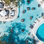Aerial view of the lagoon pool at Mrs Sippy Bali in Seminyak, with swimmers, floating daybeds and white umbrellas