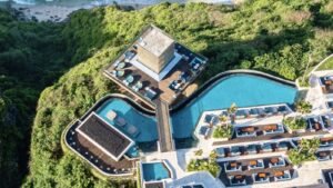 Aerial daytime view of Savaya Bali in Uluwatu showing the Cube, curved clifftop pools, daybeds and the jungle cliff down to the beach