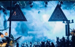 Crowd at night under illuminated triangular LED screens and smoke at Savaya Bali, Uluwatu